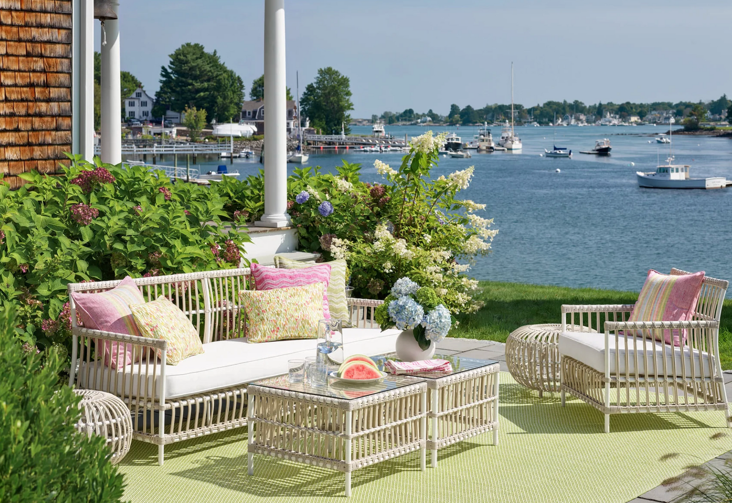 Coastal outdoor rattan seating with bright pillows overlooking harbor views – Our Boat House